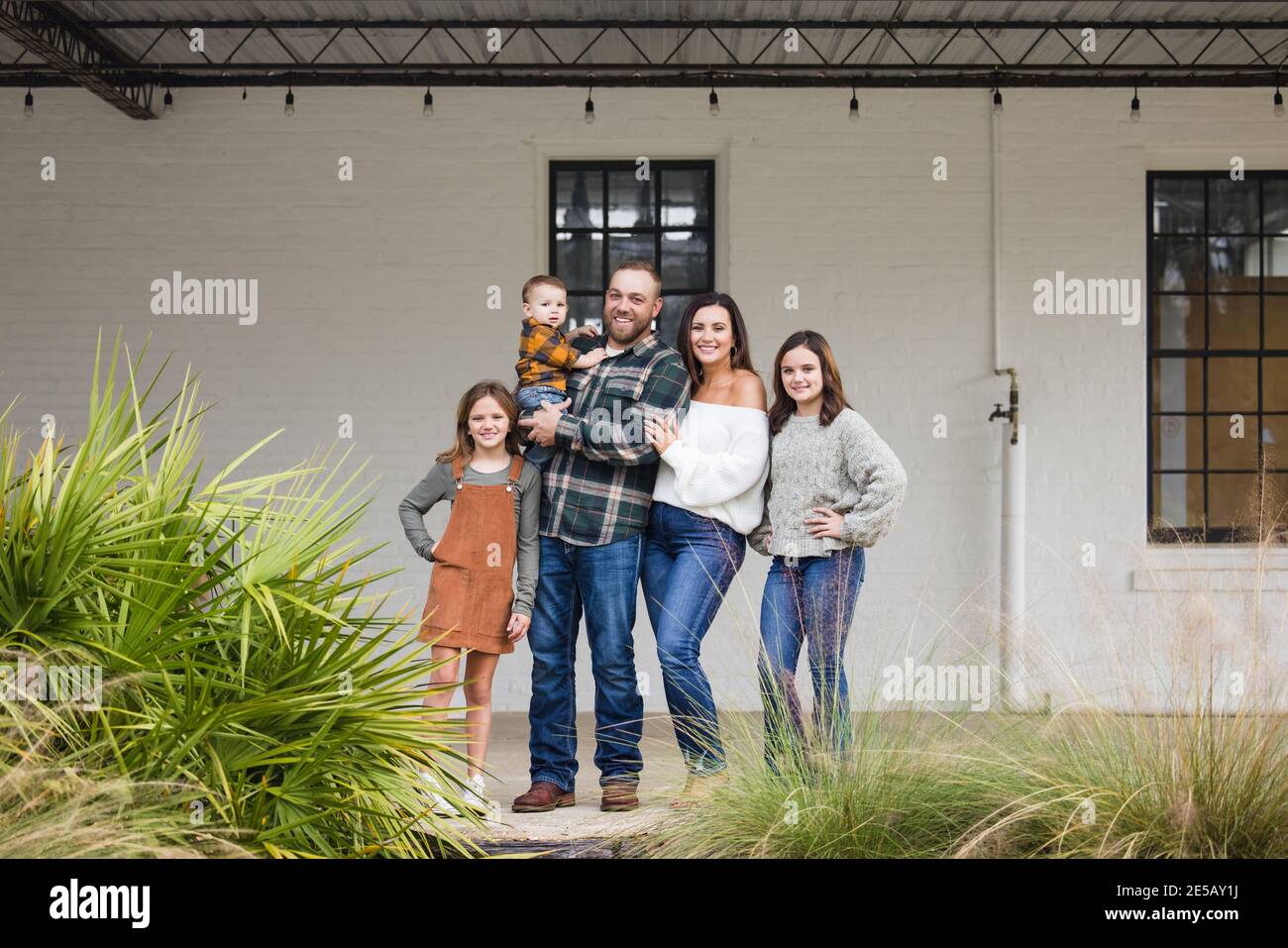 Eine fünfköpfige Familie mit zwei Mädchen und einem Baby Junge, der vor einem einfachen weißen Backsteingebäude steht Stockfoto