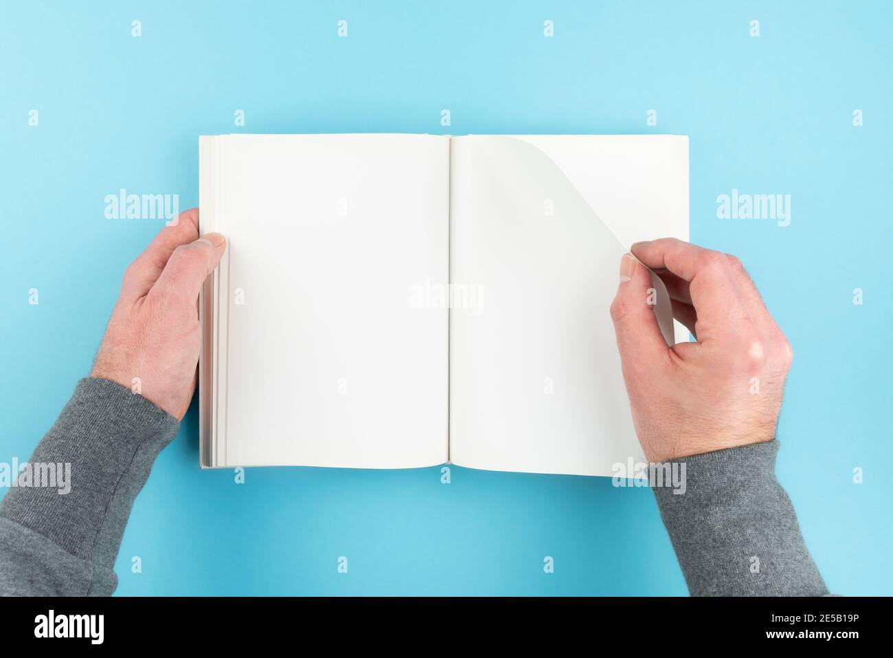 Direkt über Ansicht der Person, die Seite von blank weiß dreht Seite Hardcover Buch auf blauem Hintergrund Stockfoto