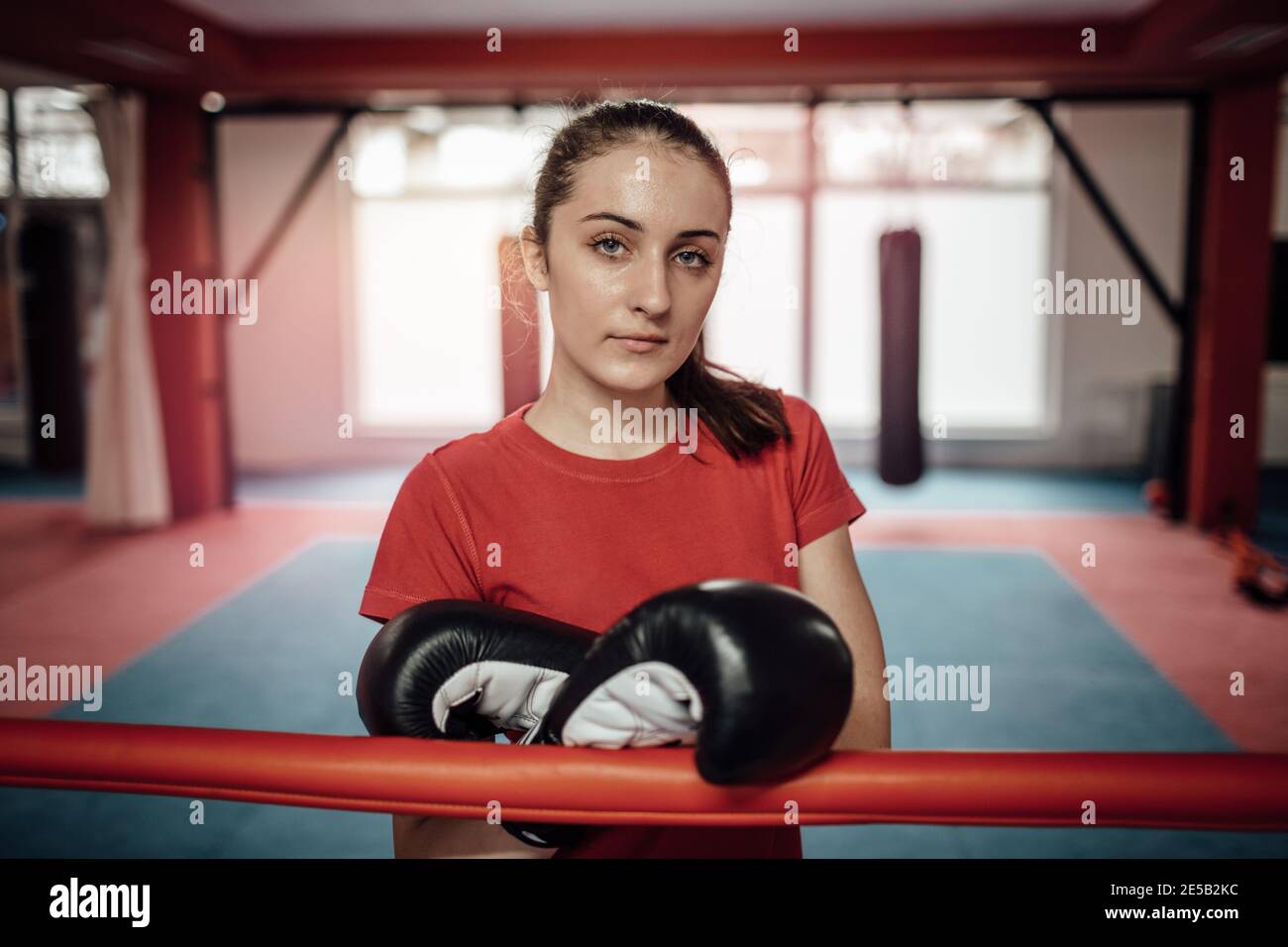 Eine Sportlerin, die nach einem Training im Fitnessstudio Boxhandschuhe trägt. Ein Porträt einer jungen Frau, die nach einer schwierigen Kickboxen-Klasse schwitzt und mich schaut Stockfoto