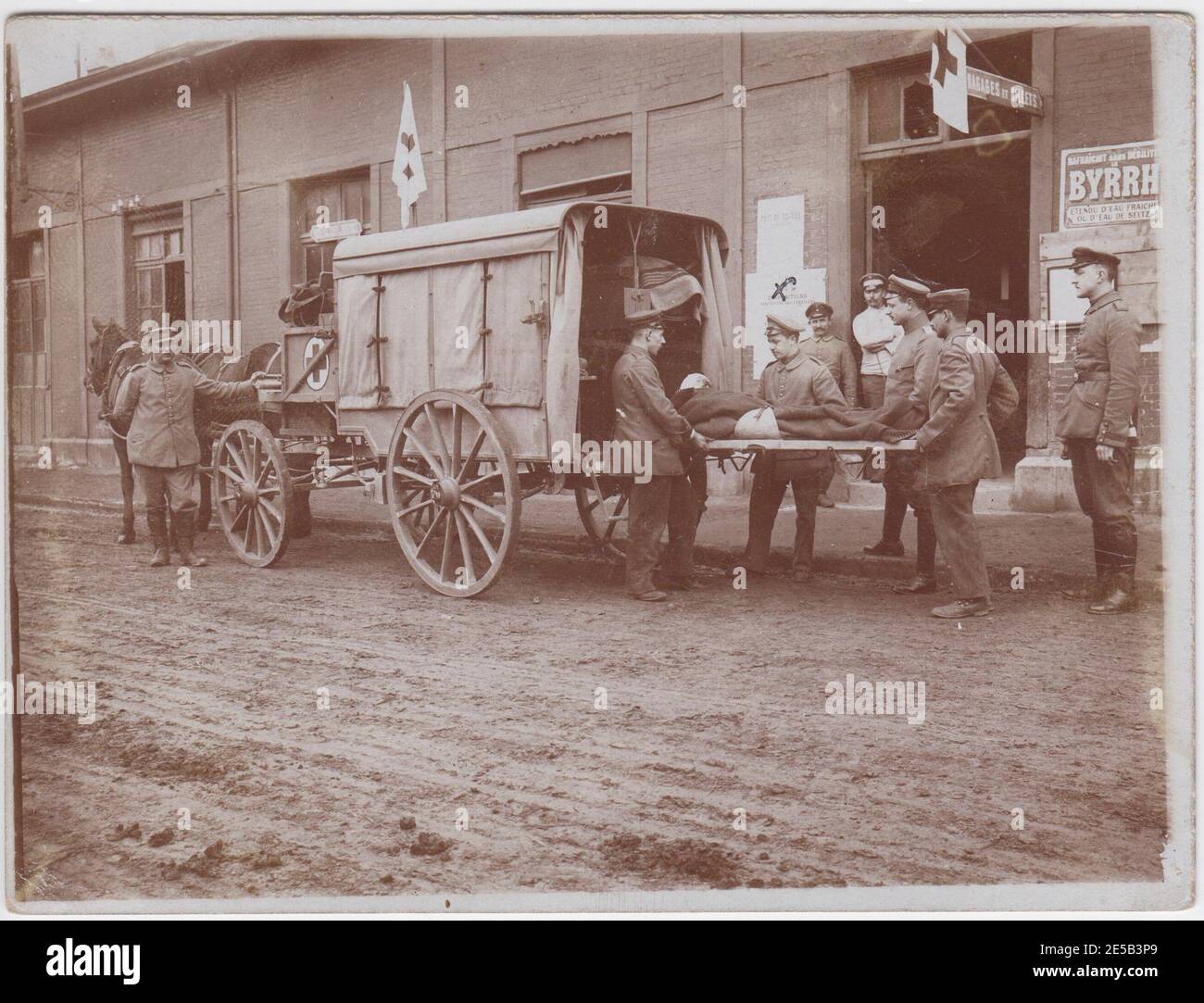 Verwundeter Soldat auf einer Bahre, von Bahre Träger in einem Pferd gezogenen Krankenwagen geladen. Sie sind vor einem Gebäude mit roten Kreuz Fahnen geparkt, die Straße ist ein breiter Schlammweg. Stockfoto