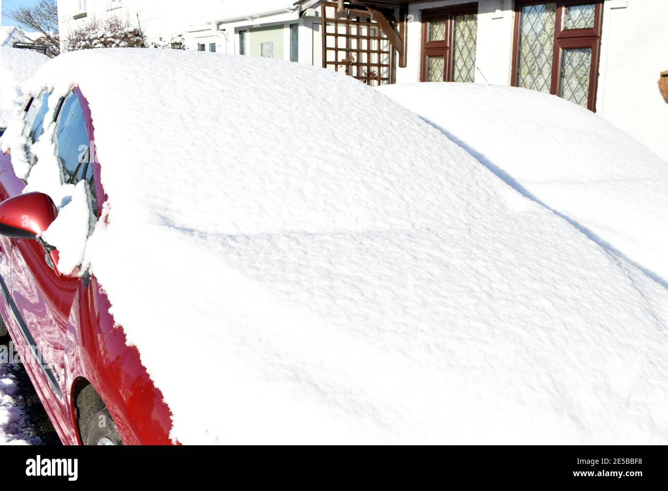 Nahaufnahme von Windschutzscheiben und Motorhauben, die an einem sonnigen kalten Wintertag mit starkem Schnee bedeckt sind. Das Auto ist vor dem Haus geparkt Stockfoto