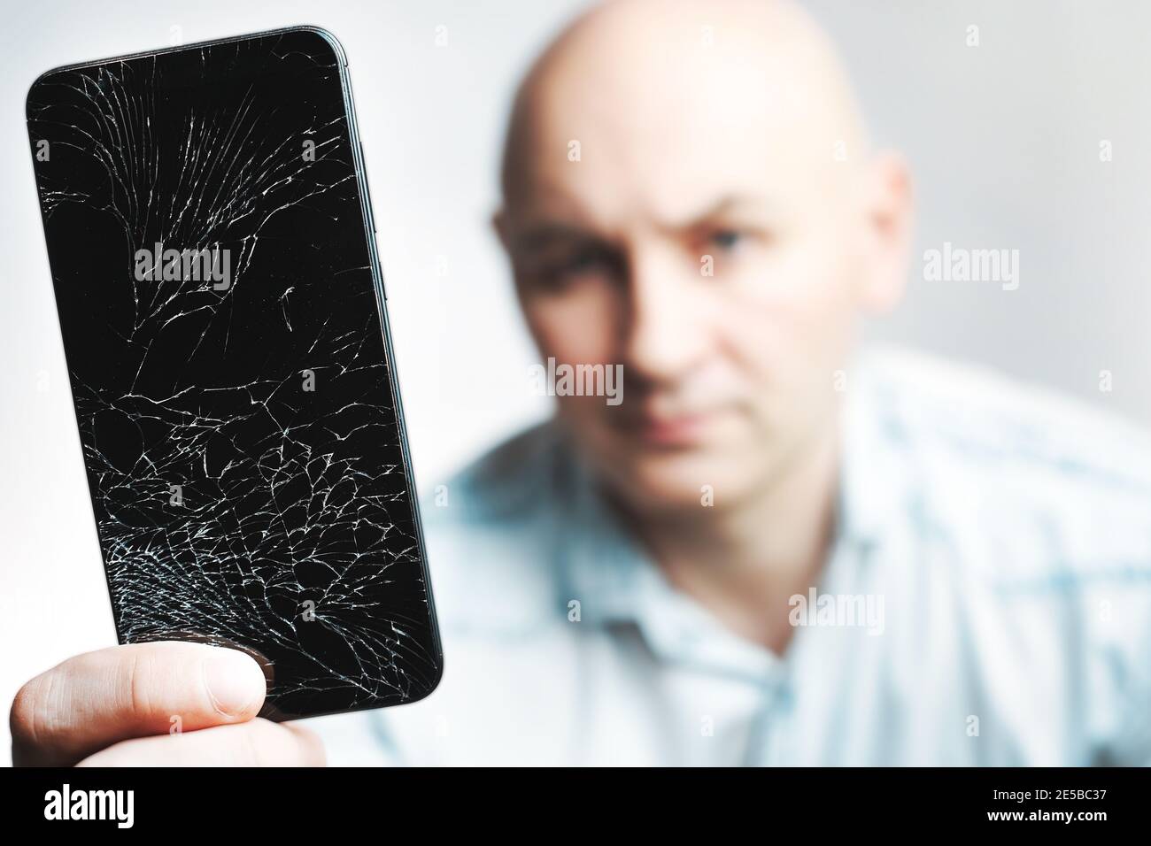 Telefon mit EINEM defekten Bildschirm Nahaufnahme. Ein weißer Mann hält ein schwarzes Smartphone mit einem geknackten Display. Stockfoto