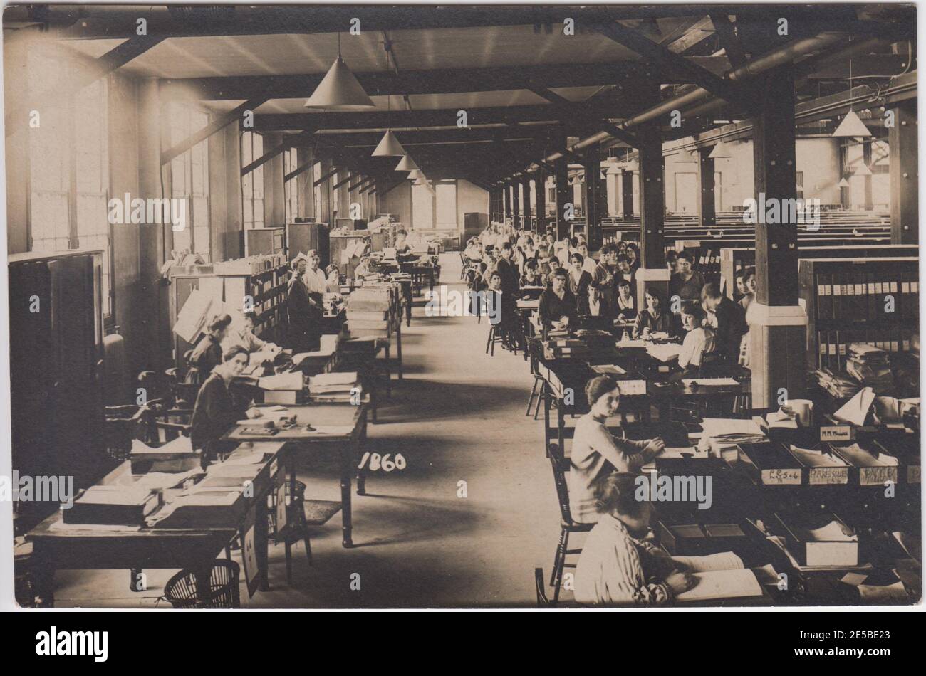 Großes Industriebüro mit Büroangestellten an ihren Schreibtischen, mit Kästen und Schränken zum Ablegen an der Seite. Die meisten Angestellten sind Frauen. 1900er/1910er Stockfoto