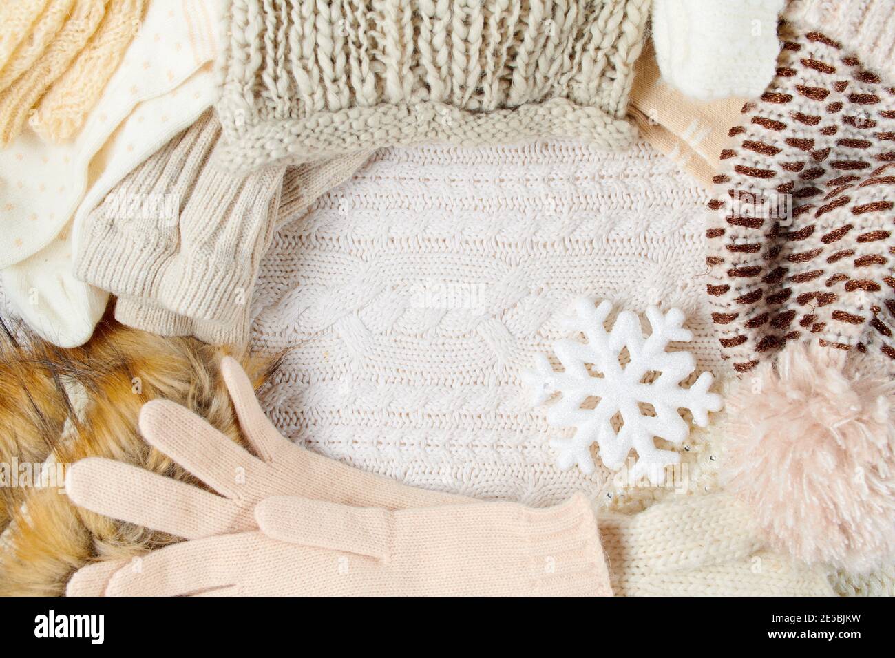 Winterflachlage mit Schneeflocke, Fäustlingen, Hüten und Winterkleidung auf weißem Strickhintergrund. Stockfoto