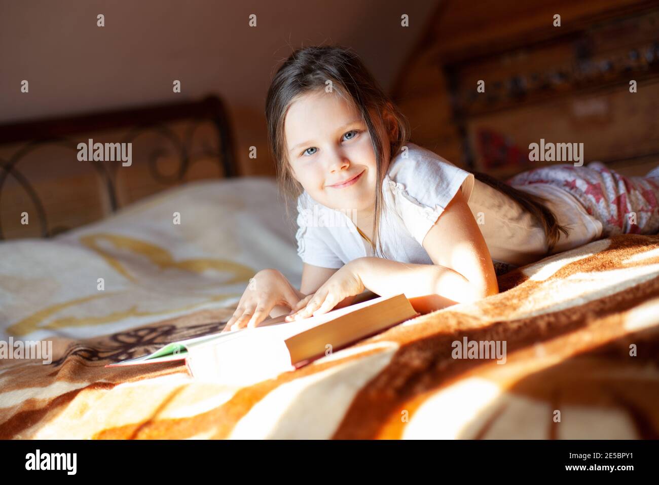 Nahaufnahme ein lächelndes, glückliches Mädchen liegt auf dem Bauch auf einer Decke auf dem Bett und liest ein Buch im Schlafzimmer einer Blockhütte im Dorf Stockfoto