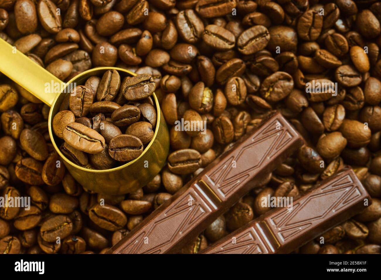 Kaffeebohnen im Messlöffel und Schokolade auf einem Hintergrund von frisch geröstetem Kaffee, geringe Schärfentiefe Stockfoto