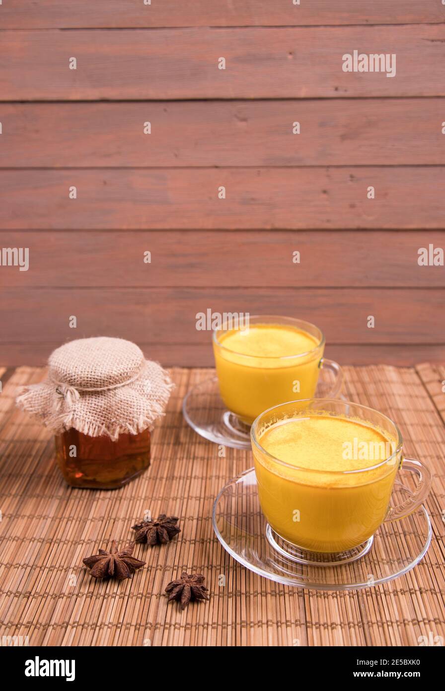 Zwei Tassen goldene Milch mit Honig und Sterne Anis auf einer Strohmatte. Veganes Getränk. Stockfoto