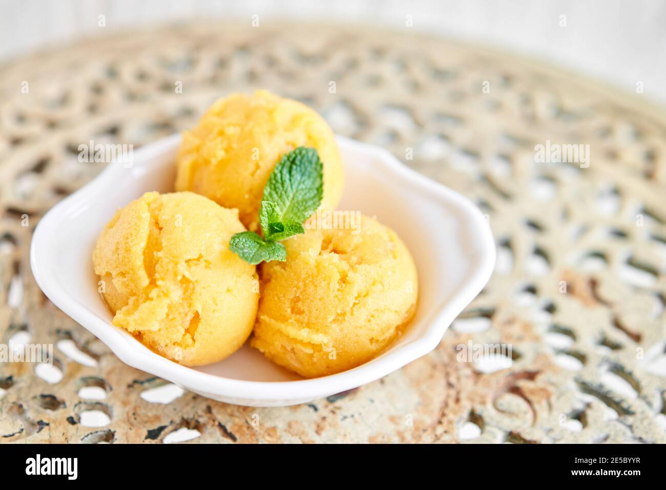 Mango-Eis mit Minzblatt. Drei Kugeln in einer weißen Schüssel auf einem Vintage-Tisch. Sorbet Stockfoto