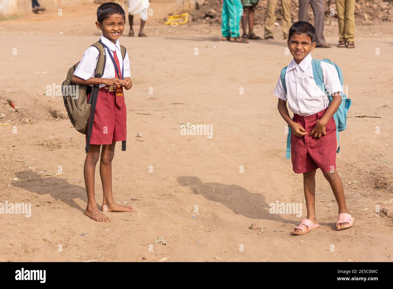 Nandakeshwar, Karnataka, Indien - 7. November 2013: Nahaufnahme von 2 jungen Jungen gehen in kastanienbraunen Shorts und weißen Hemden auf beigefarbenem Sandweg zur Schule. Stockfoto