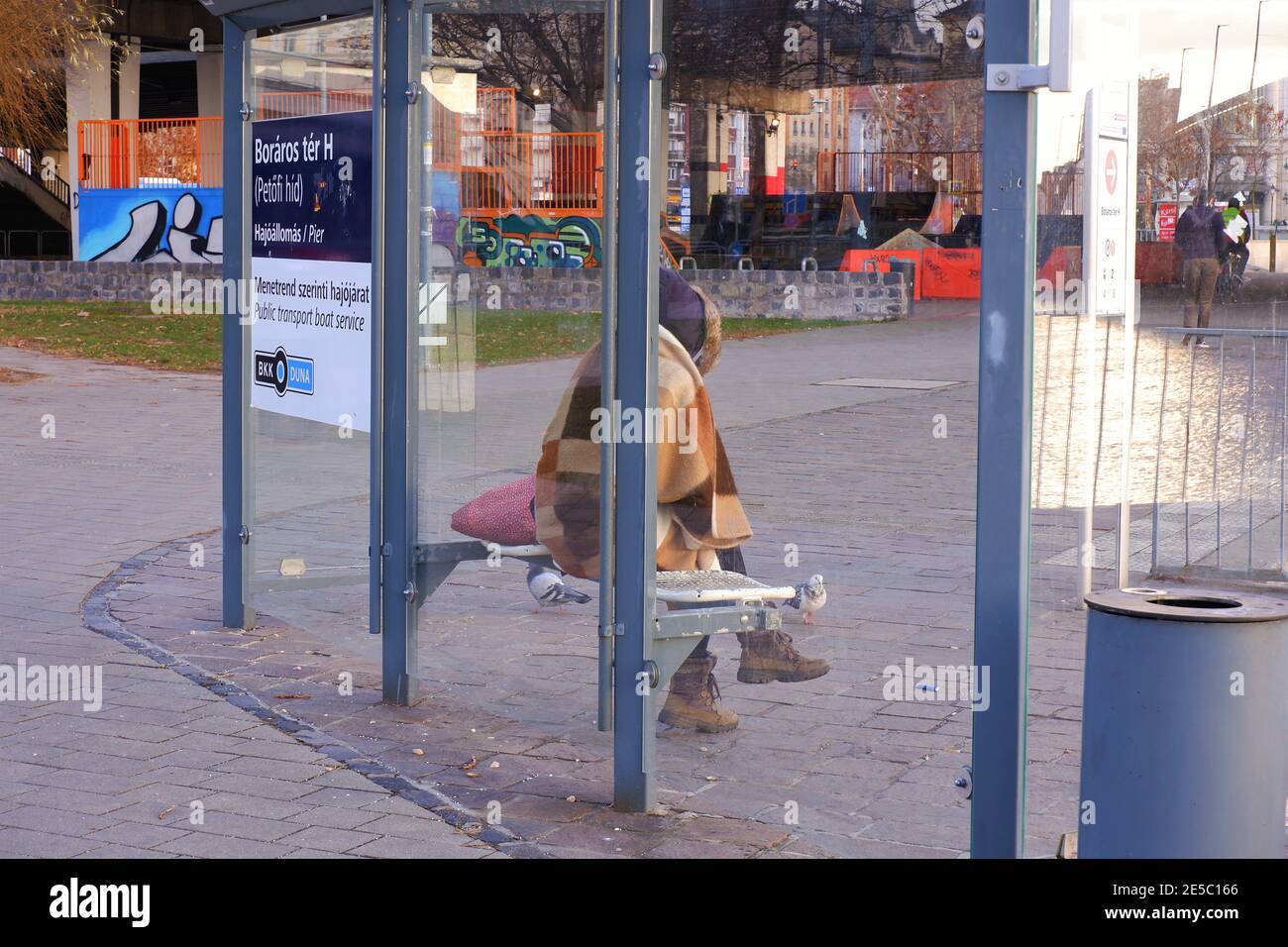 Budapest, Ungarn - 27. Januar 2021: Obdachlose Frau in einer Decke gehüllt sitzen an einer öffentlichen Hafenstation im kalten Winter Stockfoto Budapest, Ungarn - 27. Januar 2021: Obdachlose Frau in einer Decke gehüllt sitzen an einer öffentlichen Hafenstation im kalten Winter Stockfoto