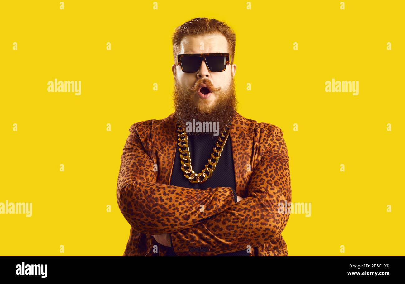Exzentrischer bärtiger Mann in Jacke mit Leopardenmuster und goldenem Hals Gekreuzte Kette mit stehenden Armen Stockfoto