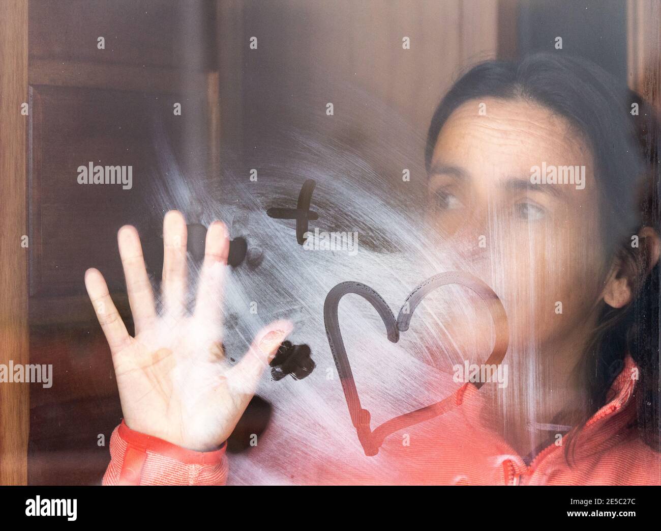 Frau mittleren Alters, die aus dem Fenster schaut. Kondensation am Fenster. Stockfoto