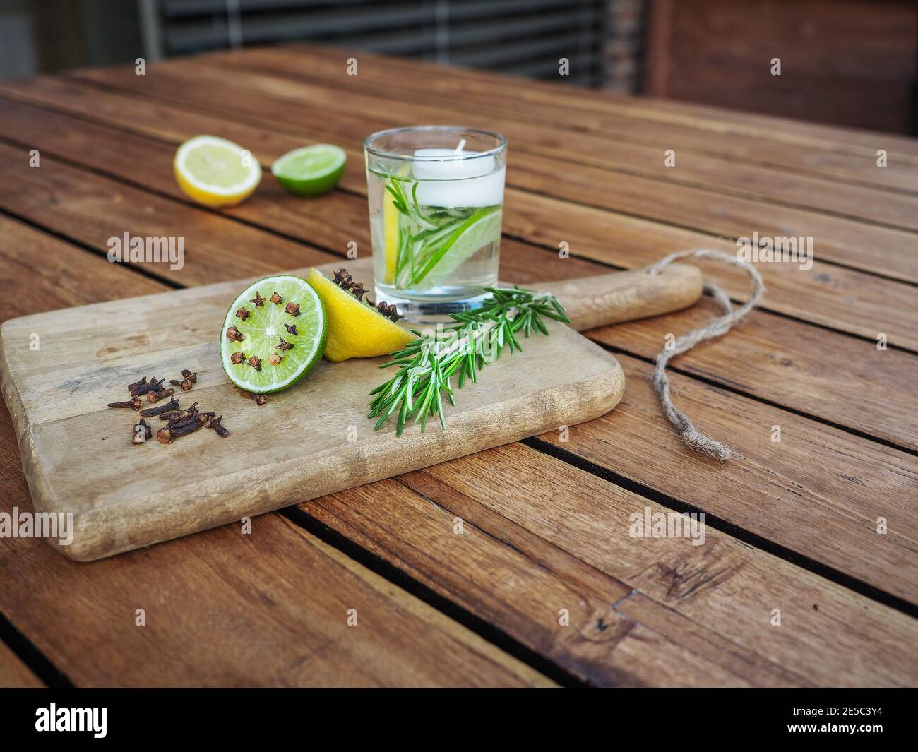 Natürliche hausgemachte Repellents auf Holztisch. Limette und Zitrone mit Nelken. Limette und Zitrone, Teelicht Kerzen, frischer Rosmarin und Wasser. Stockfoto