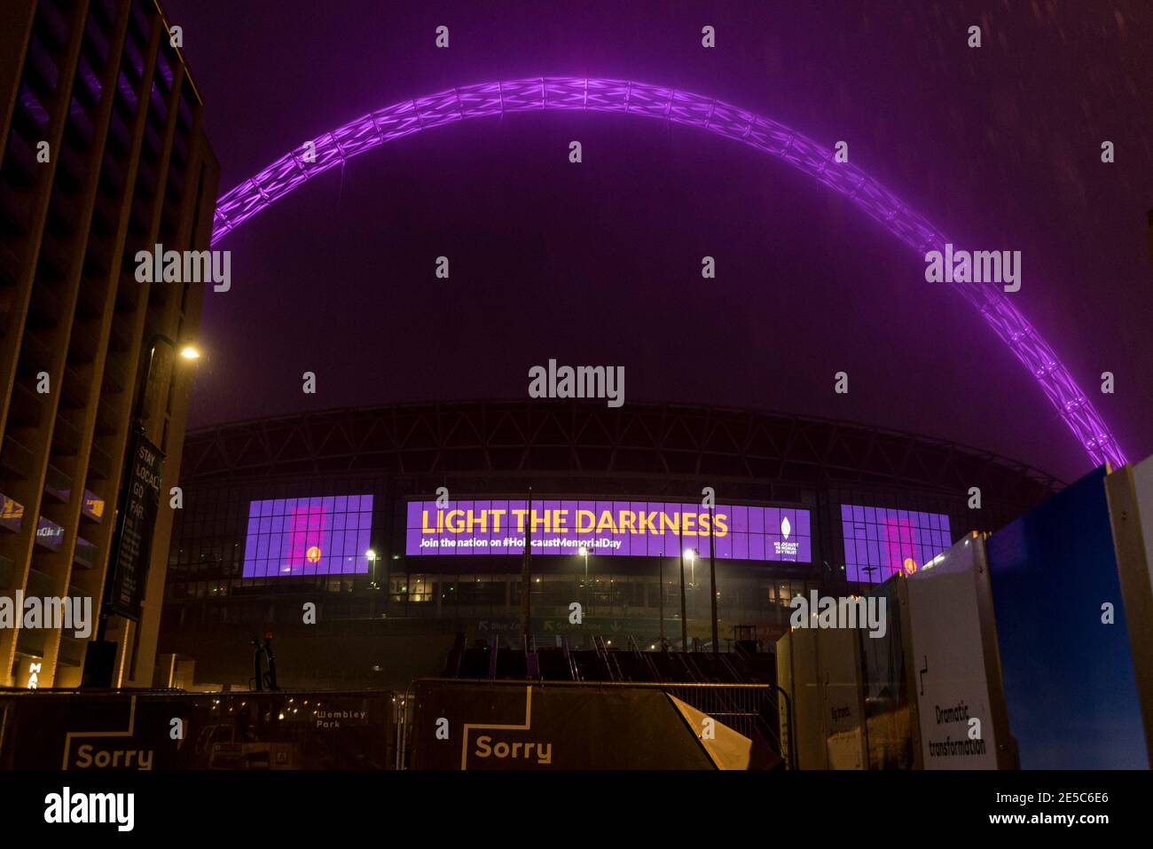 London, Großbritannien. 27. Januar 2021. Bei starkem Regen werden das Wembley-Stadion und sein Bogen am Holocaust-Gedenktag, einem Tag, der den Völkermord an sechs Millionen Juden und anderen Minderheiten während des Zweiten Weltkriegs durch die Nazis markiert, in Purpur beleuchtet. 25 ikonische britische Wahrzeichen wurden nach dem diesjährigen Thema „Be the Light in the Darkness“ beleuchtet. Aufgrund der Covid-19-Pandemie wird eine Zeremonie zur Erinnerung an die Opfer online stattfinden, die von Boris Johnson, Premierminister, und seiner Königlichen Hoheit Prinz von Wales unterstützt wird. Kredit: Stephen Chung / Alamy Live Nachrichten Stockfoto