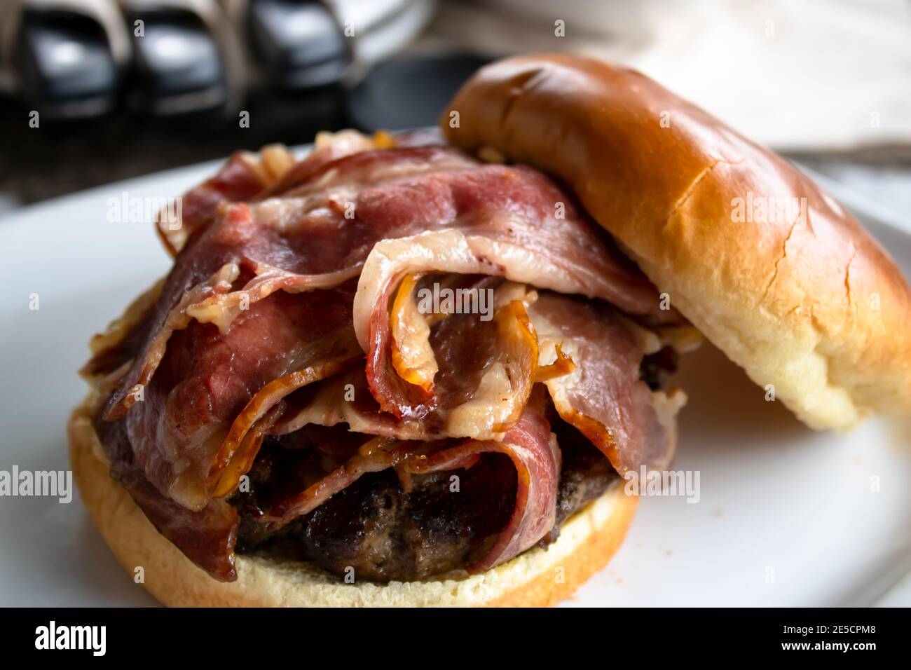 Seitenansicht Nahaufnahme eines Bacon Burger mit dem Oberes Brötchen, das auf einer weißen Platte abrutscht Stockfoto