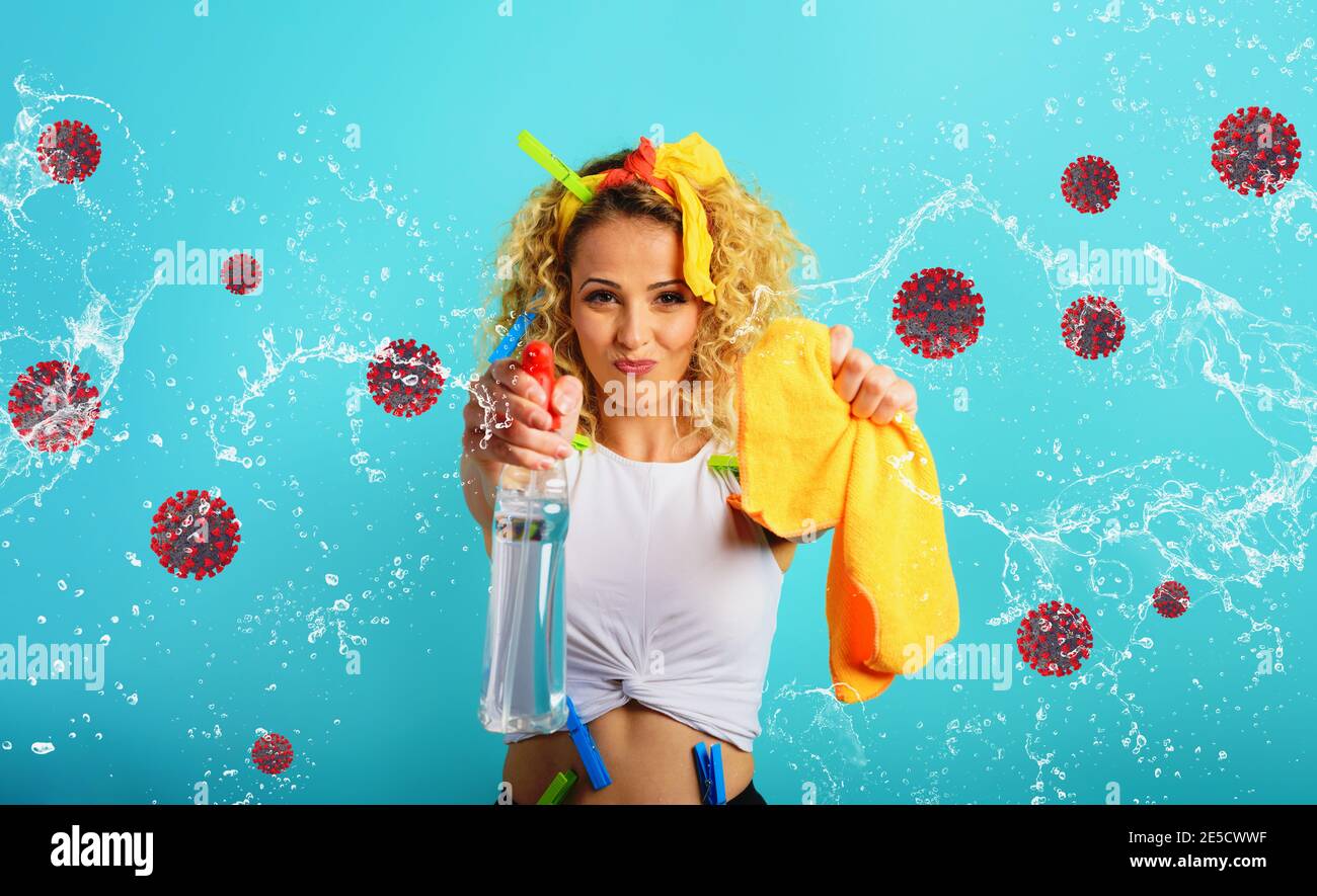 Blonde Hausfrau splashs Desinfektionsmittel, um Viren und Bakterien von covid-19 zu entfernen. Cyanfarbener Hintergrund Stockfoto