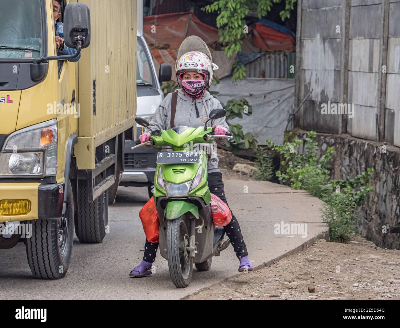 Jakarta, Indonesien - 20. Februar 2018: Frau auf einem Motorrad in einem Helm, Flip Flops und einer Gesichtsmaske auf der Straße in Jakarta. Asien. Stockfoto