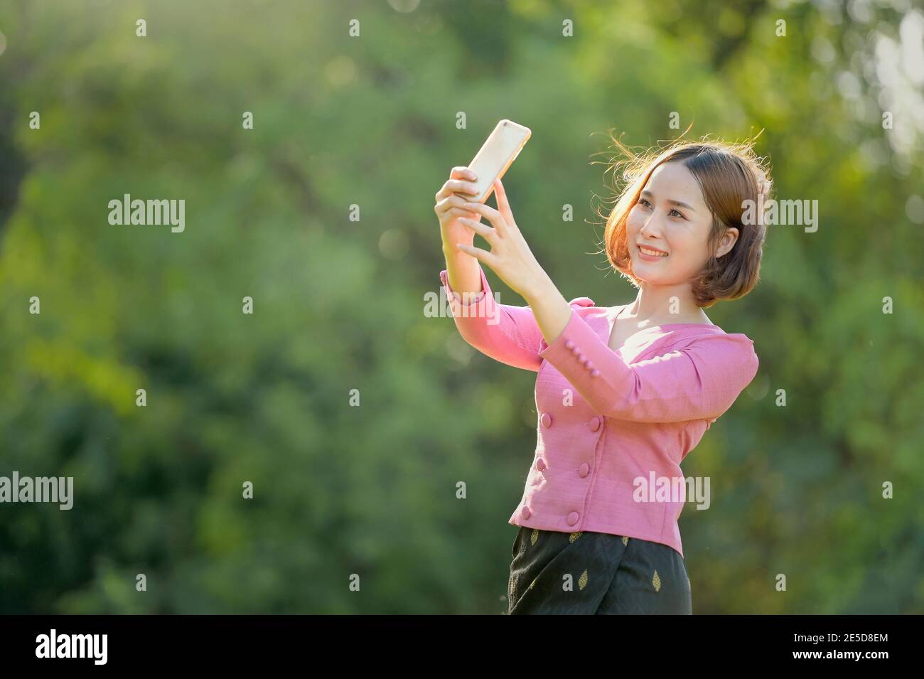 Lächelnde Frau, die in einem Garten steht und ein Selfie mit ihrem Handy macht, Thailand Stockfoto