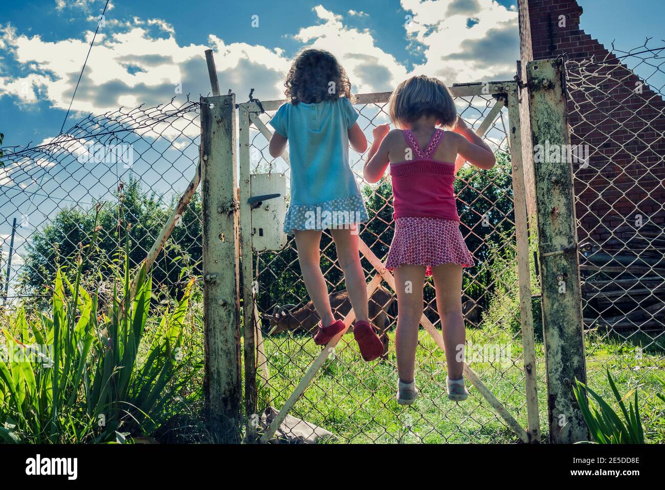 Rückansicht von zwei Mädchen, die auf einem Metallzaun klettern, Polen Stockfoto