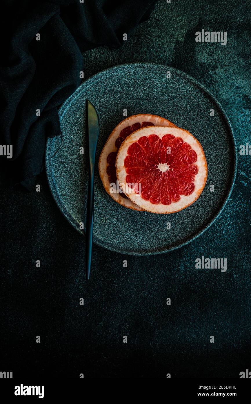 Reife rosa Grapefruitscheiben auf schwarzem Teller Stockfoto