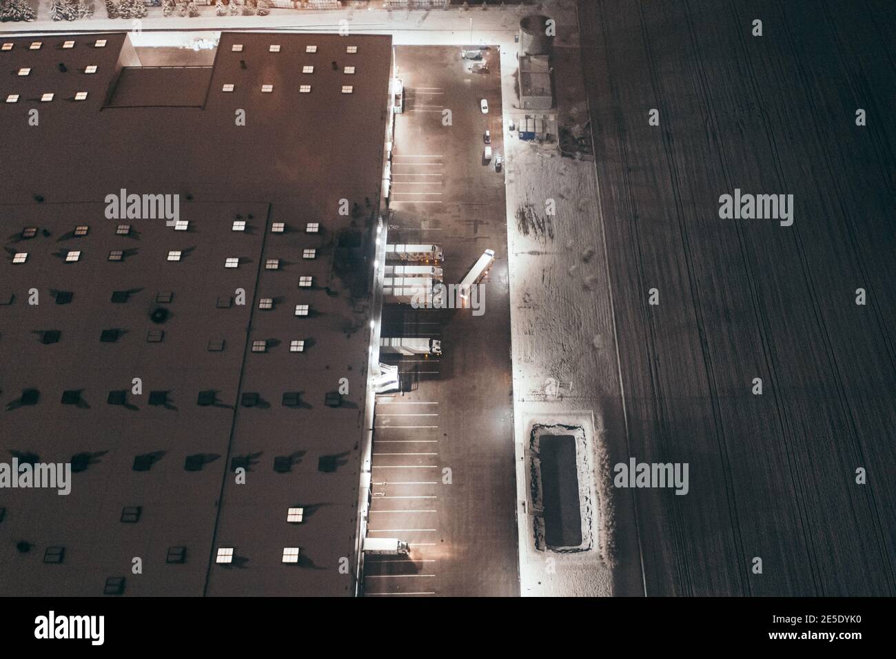 Luftaufnahme der LKW-Entladung im Logistikzentrum. Nachtansicht mit ein wenig Schnee. Stockfoto