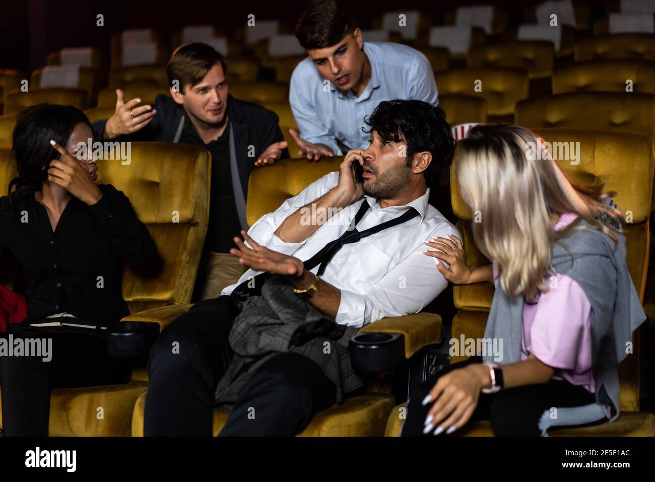 Ärgerlicher Mann, der auf dem Handy am Kinosaal mit Menschen im Kino spricht, ist wütend auf ihn Stockfoto