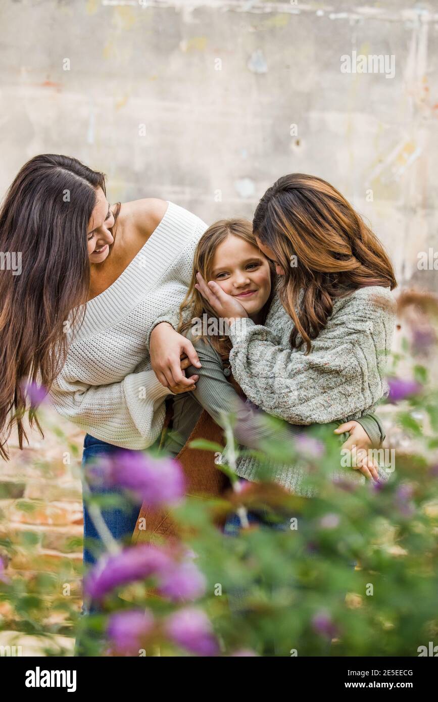 Eine junge Mutter in den 30er Jahren mit ihren beiden Töchtern Draußen umarmt und lacht zusammen Stockfoto