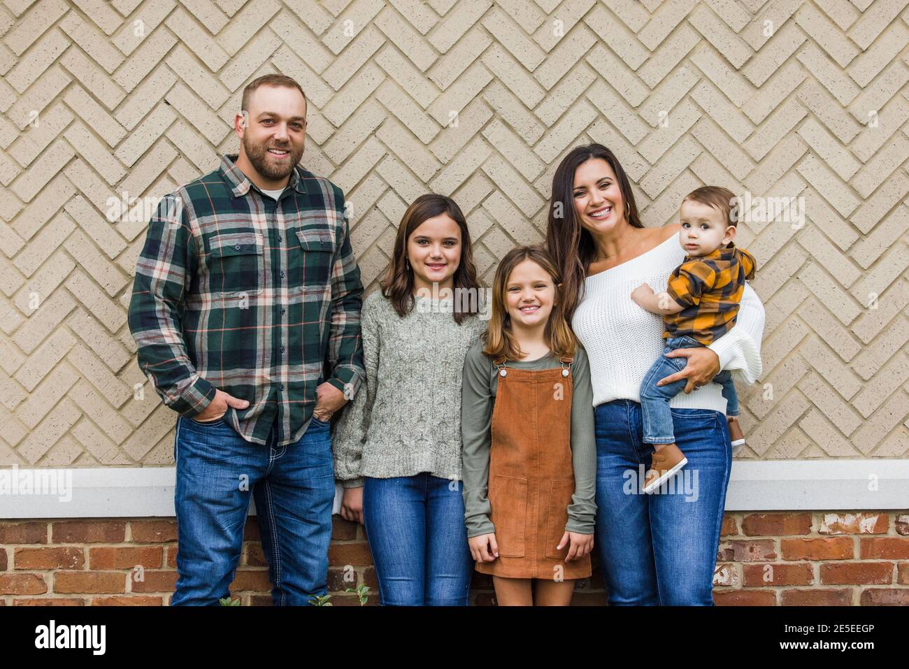 Eine fünfköpfige Familie mit zwei Mädchen und einem Baby Junge, der vor einem Ziegelsteinheringbone steht Stockfoto