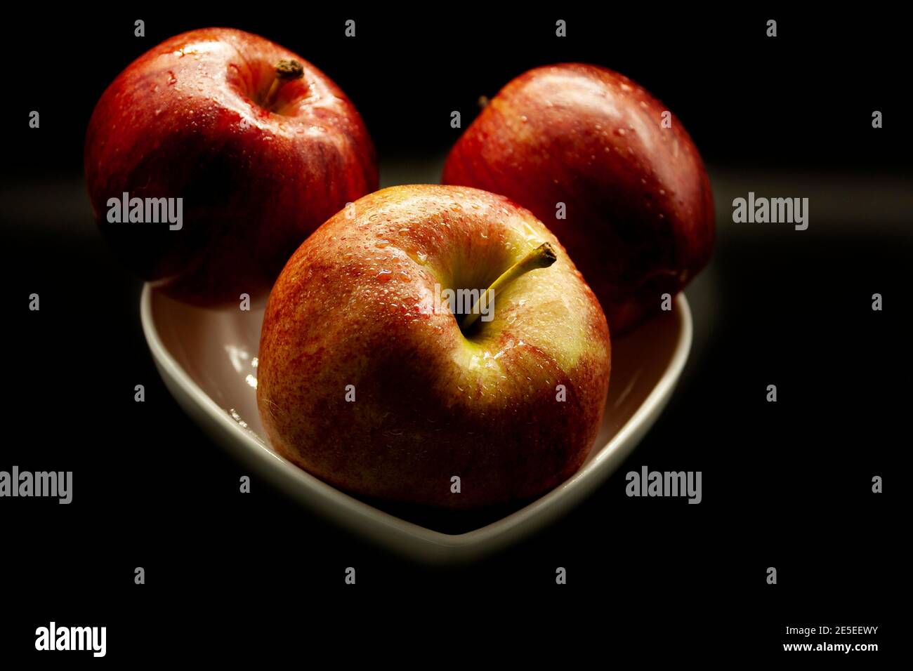 Drei frische Äpfel in einer weißen Schüssel auf einem angeordnet Schwarzer Hintergrund bereit zu essen Stockfoto