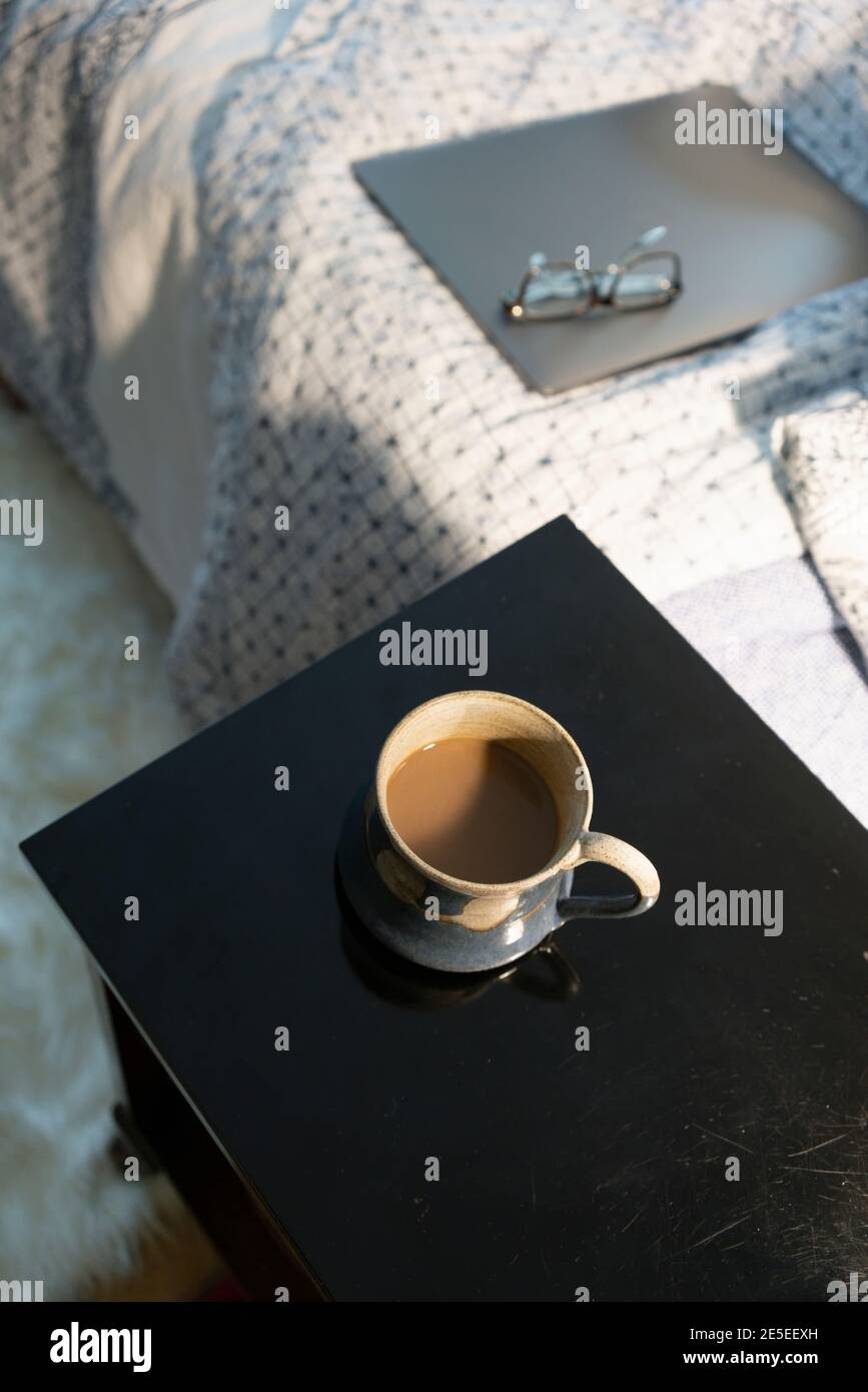 Kaffeepause Arbeiten von zu Hause Konzept geschlossener Laptop sitzt auf dem Bett mit Gläsern und einer Tasse Kaffee auf dem Beistelltisch Nachttisch, von dem aus geschossen wird Stockfoto