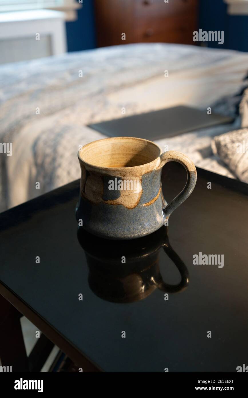 Teepause bei der Arbeit von zu Hause aus. Ein geschlossener Laptop steht auf dem Bett mit Teetasse Teetasse Tasse auf dem Nachttisch. Weitwinkelblick auf das Schlafzimmer, Büro, Stilleben Stockfoto