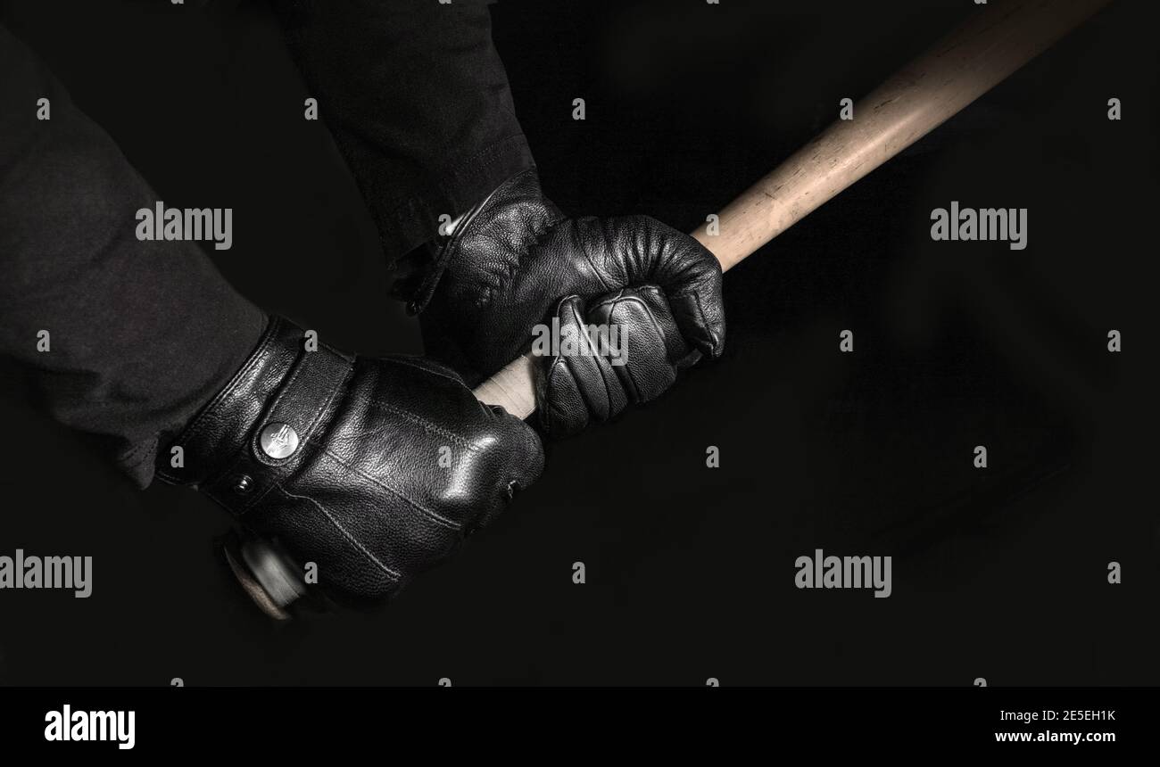 Im Dunkeln halten zwei Handschuhen einen Baseballschläger fest mit dem offensichtlichen Ziel, Chaos zu verursachen. Stockfoto