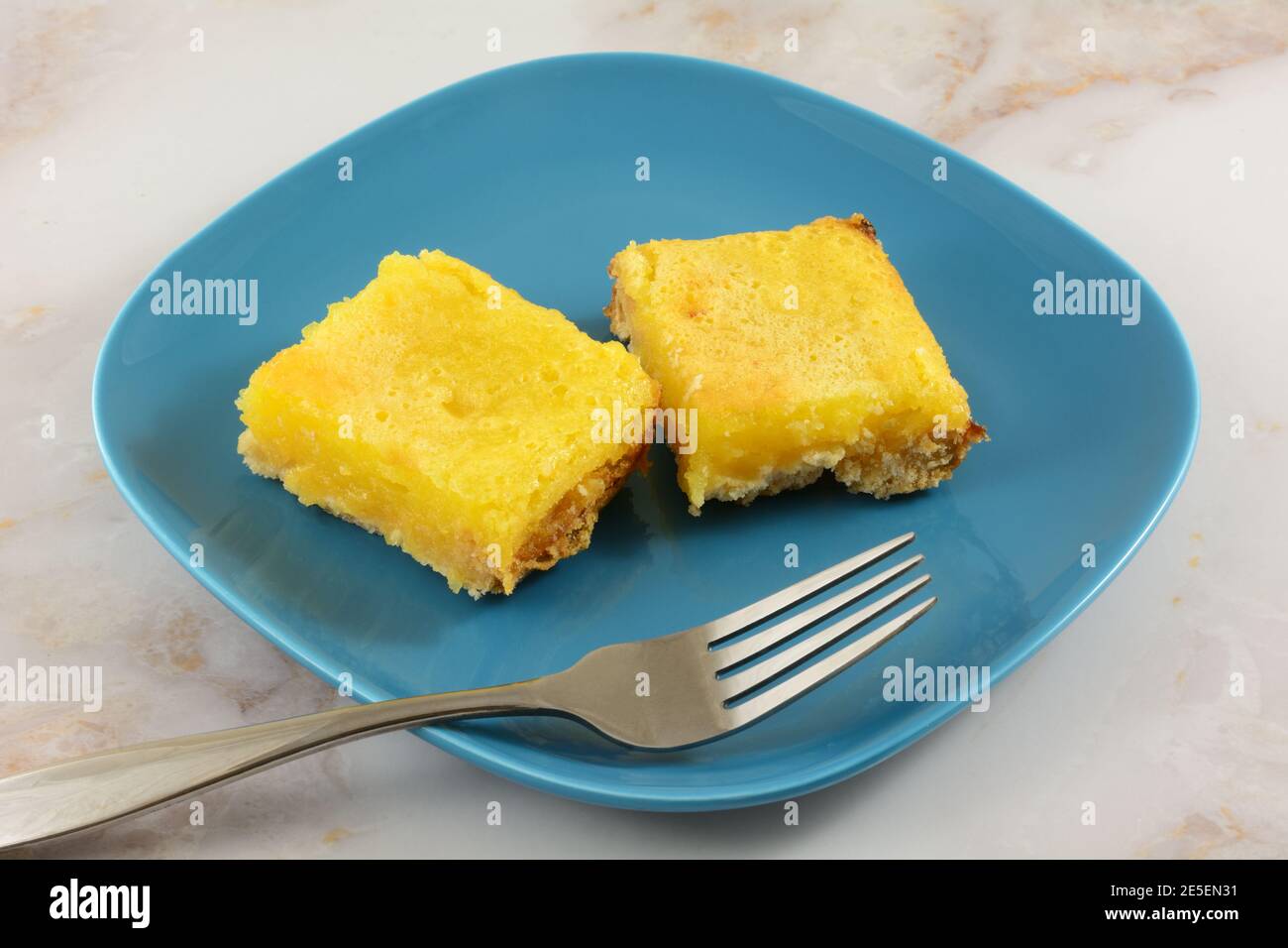 Zwei gebackene Zitronen Dessertbars auf blauem Snackteller mit Gabel Stockfoto