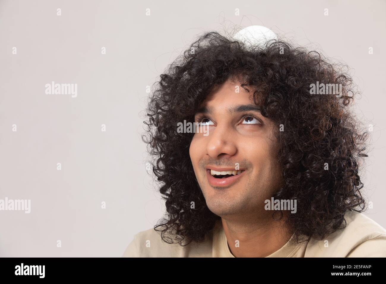 EIN GLÜCKLICHER JUNGER MANN MIT LOCKIGEN HAAREN BALANCING BALL AUF SEINEN KOPF Stockfoto