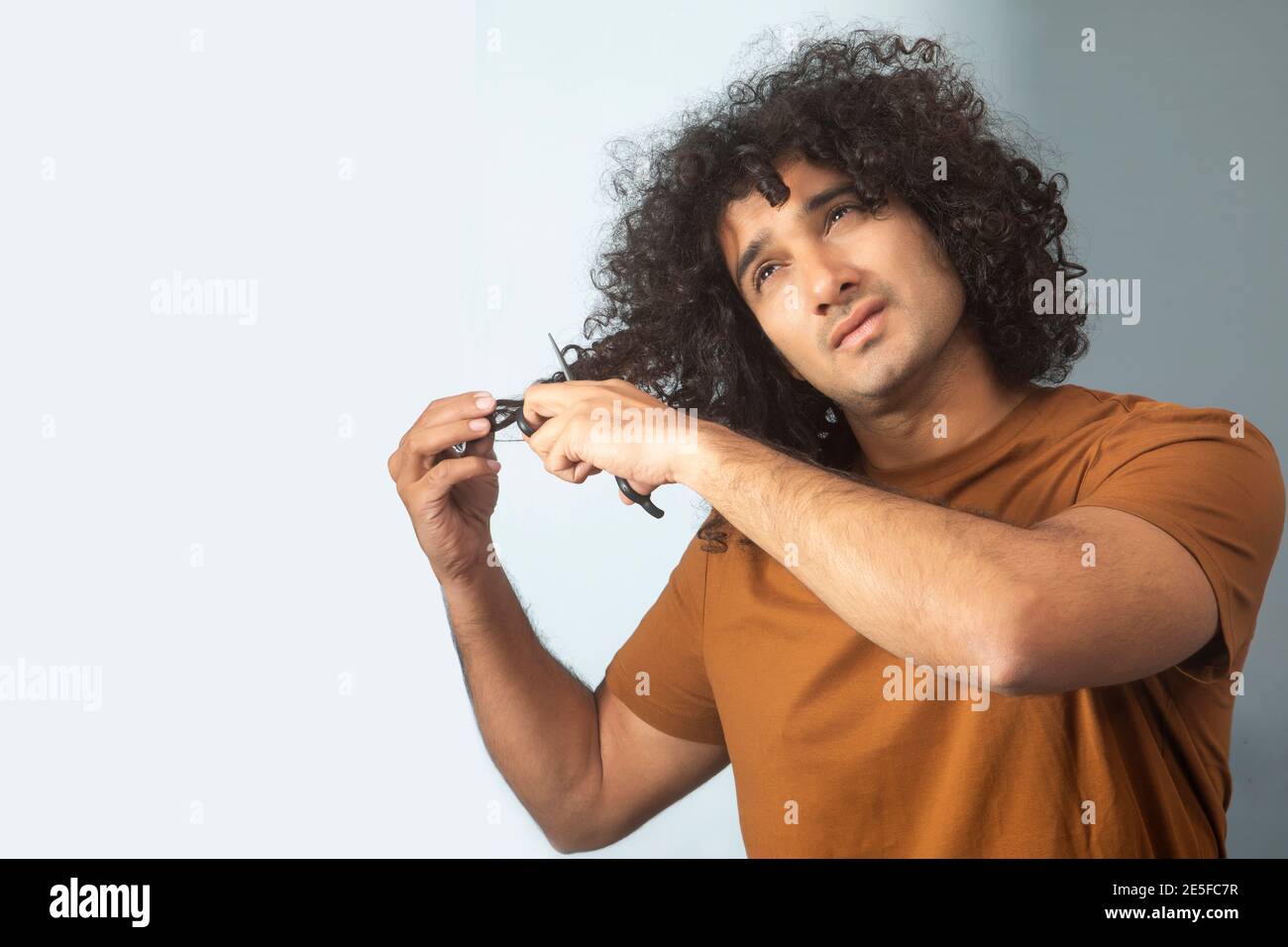 EIN JUNGER MANN MIT DICKEN LOCKIGEN HAAREN VERSUCHT ZU SCHNEIDEN EINIGE HAARSTRÄHNEN Stockfoto