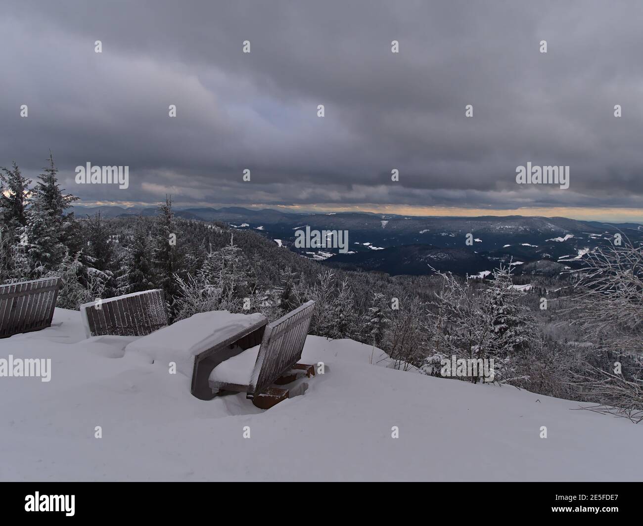Holzbänke und Tische mit tiefem Schnee und herrlichem Panoramablick über die Schwarzwälder Berge mit schneebedeckten Nadelbäumen. Stockfoto