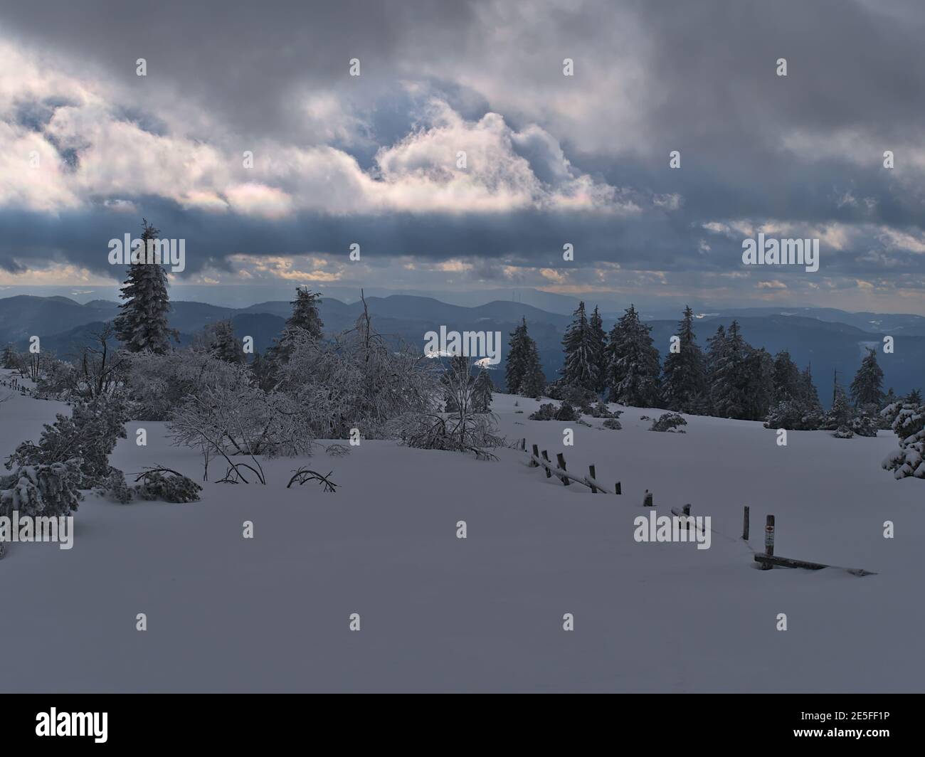 Wunderschöne Winterlandschaft mit Holzzaun bedeckt von tiefem Schnee, gefrorenen Bäumen und herrlichem Panoramablick über die Niedergebirge Schwarzwald. Stockfoto