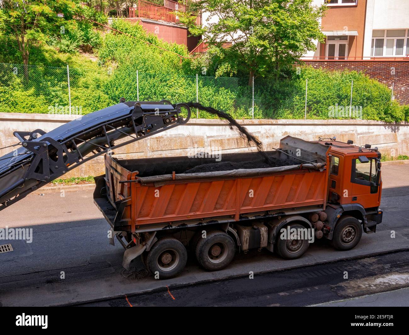 Die Fräsmaschine entfernt alten Asphalt von der Straße und transportiert ihn zu einem LKW. Stockfoto