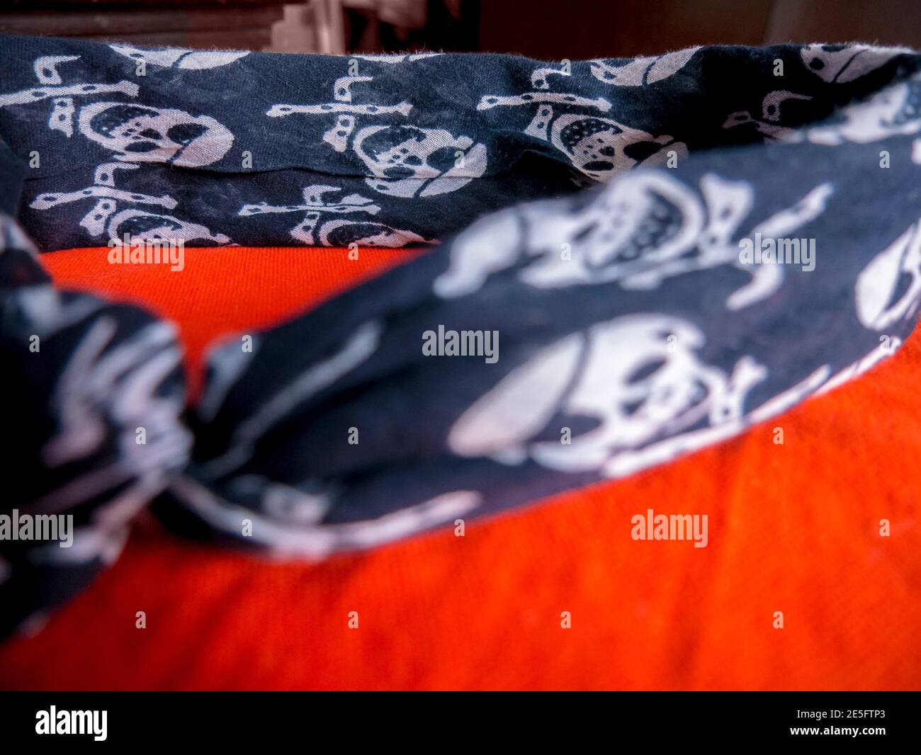 Schal mit Totenkopf und Kreuzknochen wie ein Stirnband darauf liegend Orangefarbenes Tuch – selektiver Fokus Stockfoto
