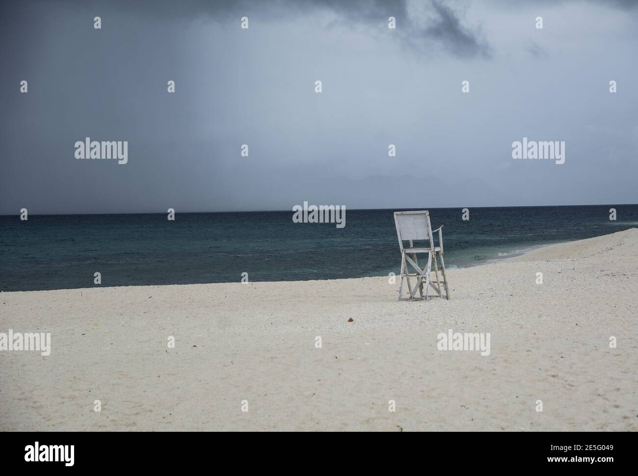Ein einsamer Stuhl vor dem Meer auf einem Weißer Strand unter schwarzen Wolken Stockfoto