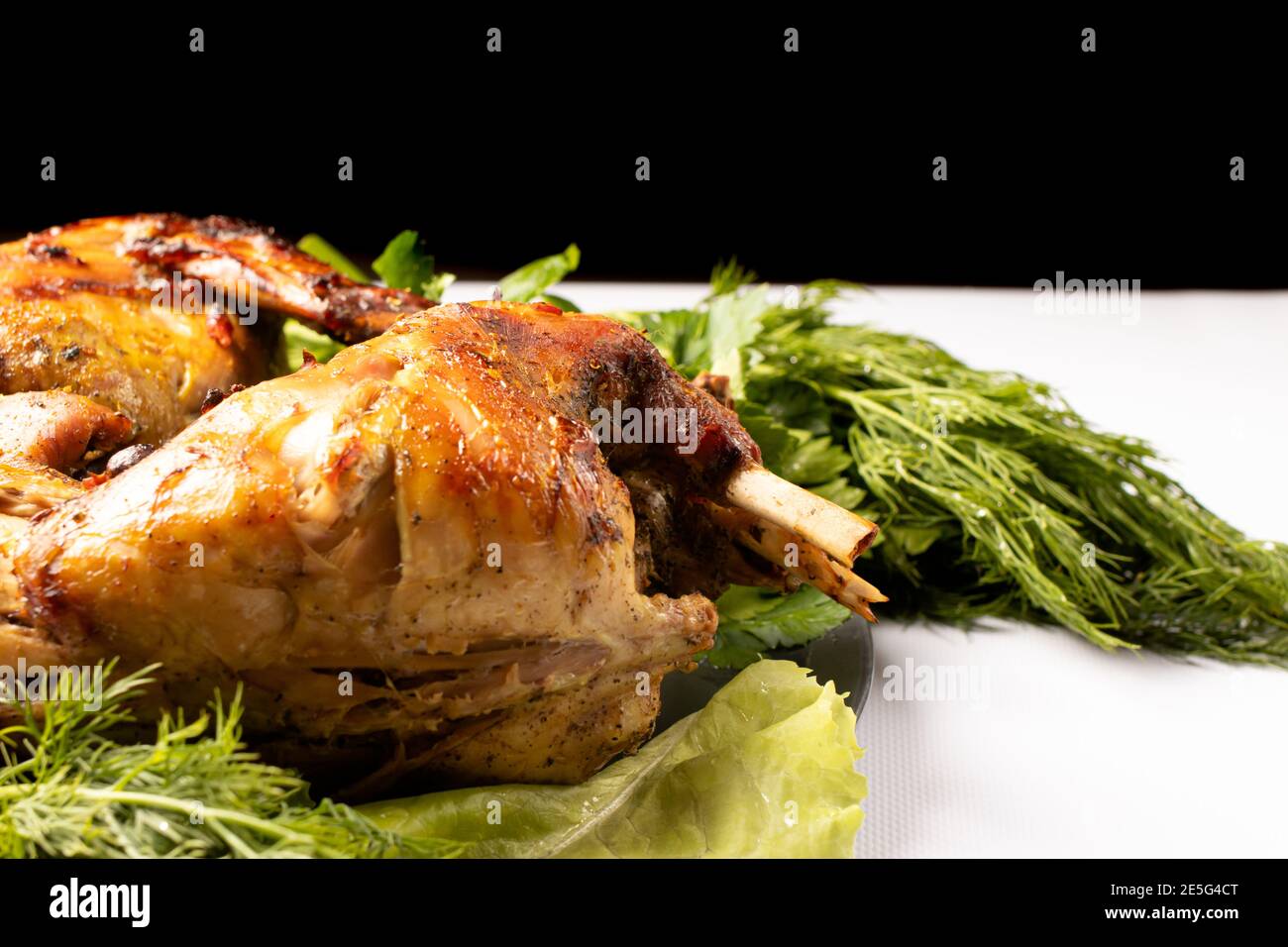 Kaninchenfleisch mit Gemüse und Kräutern auf einem Teller gebacken Auf einem schwarz-weißen Hintergrund Stockfoto