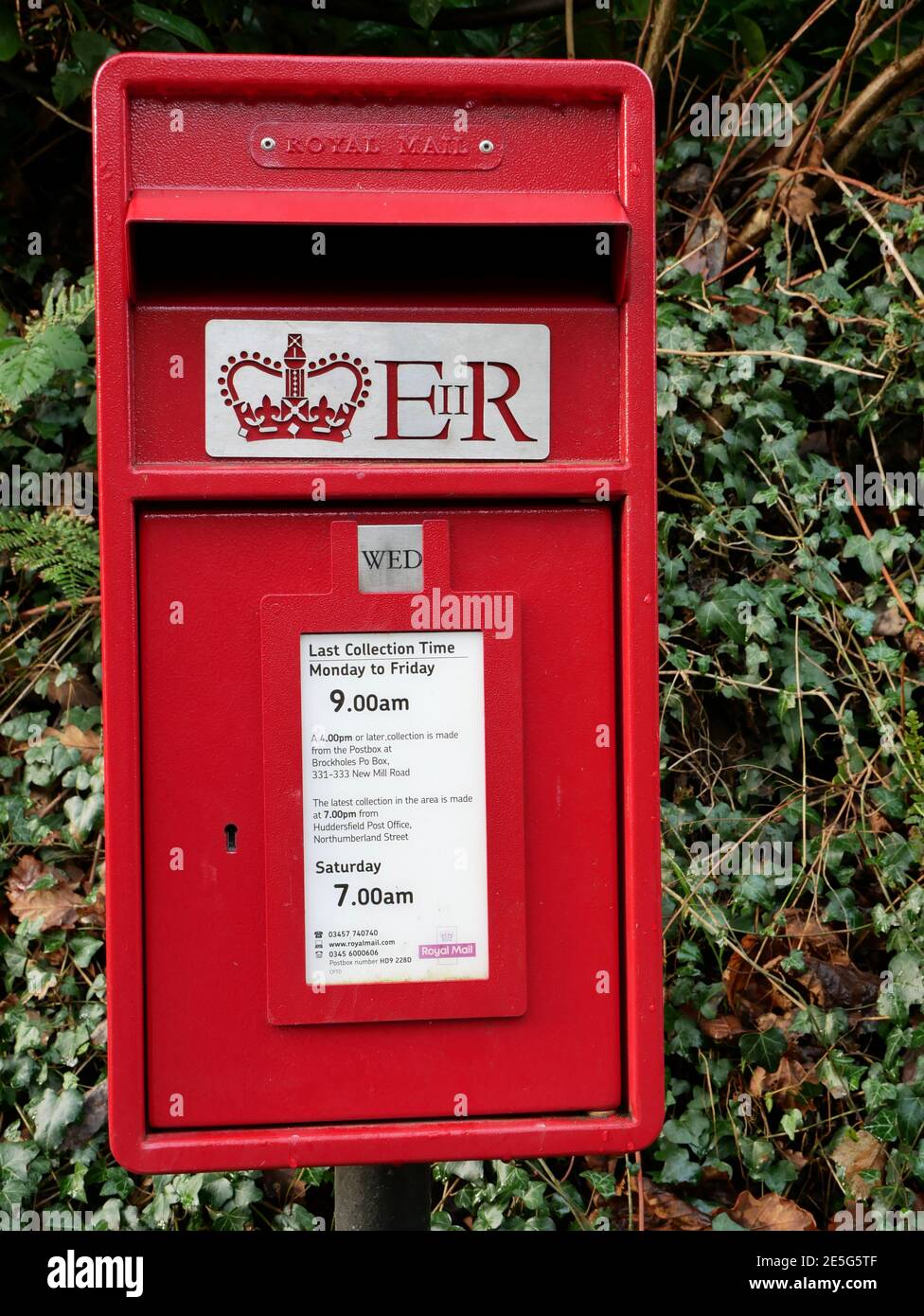 Kleiner roter Briefkasten auf runder Metallpfosten mit Laub Im Hintergrundbild von Krone und E 11 R Stockfoto