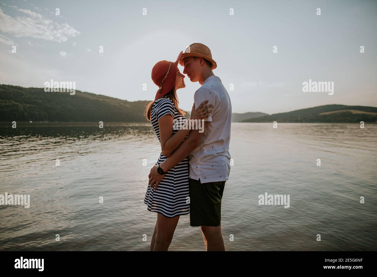 Ein verliebten Paar umarmt am Strand bei Sonnenuntergang. Portrait von jungen Mann und Frau, die sich gegenseitig in die Augen schauen am See gegen die Abendsonne. Stockfoto