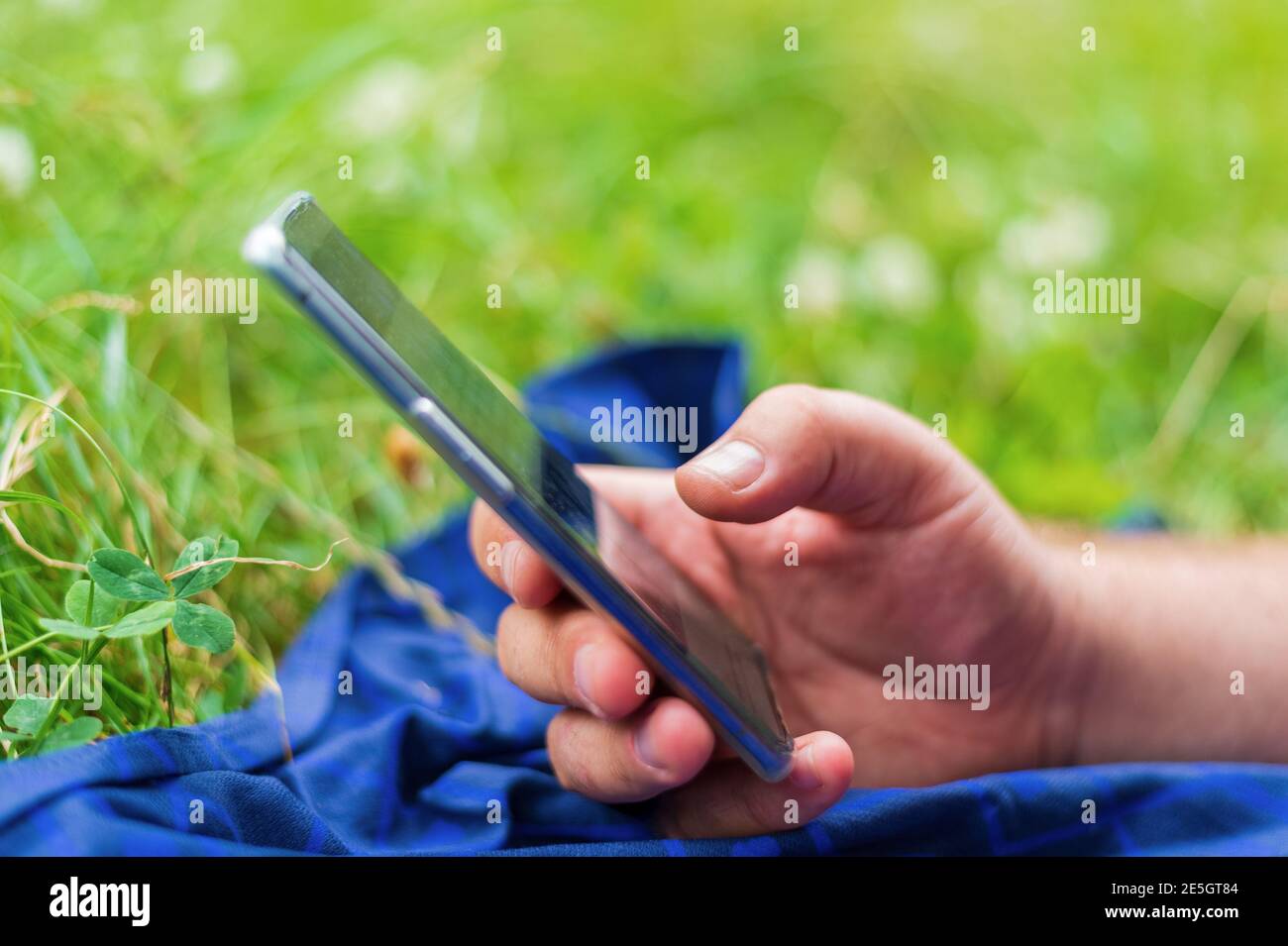 Erwachsener Mann hält Smartphone, während auf grünem Gras in liegen Stadtpark Stockfoto