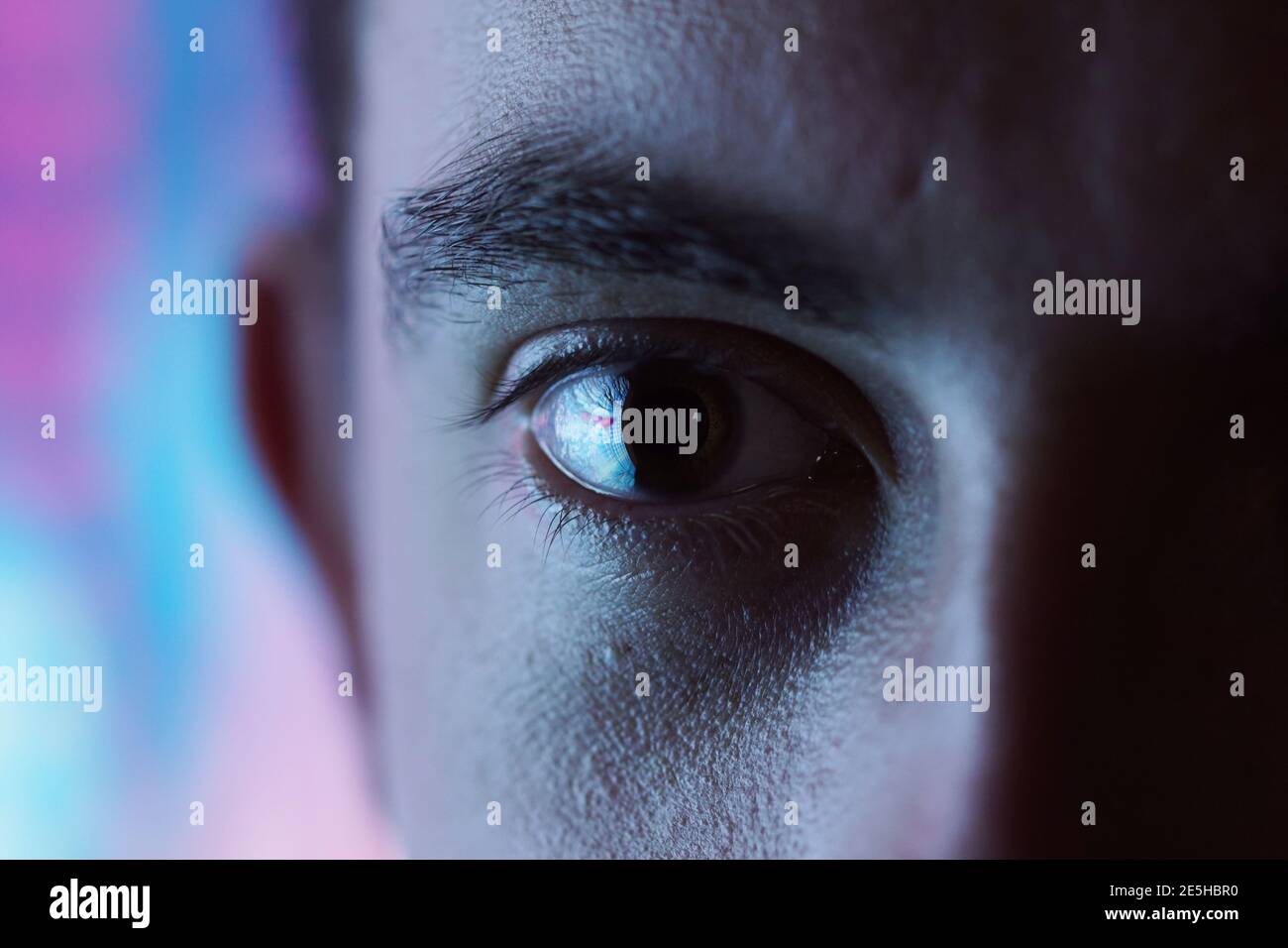 Ausdrucksstarke Optik - Nahaufnahme des Auges mit verschwommenem Blau Und rosa Neonlicht Hintergrund und hohen Kontrast Stockfoto