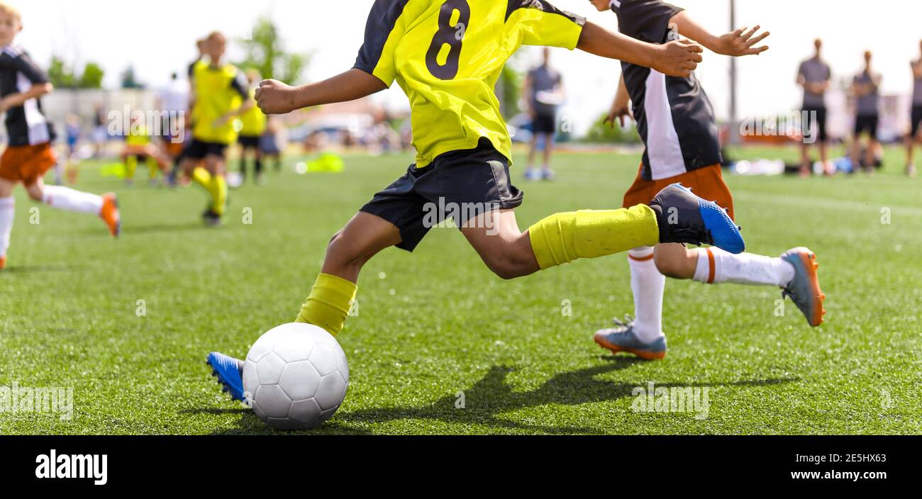 Junger afrikanischer Fußballspieler läuft schnell und tritt weißen Fußball. Jugendfußballer treten im Turnierspiel an. Fußball-Sportler tritt Ball. Stockfoto