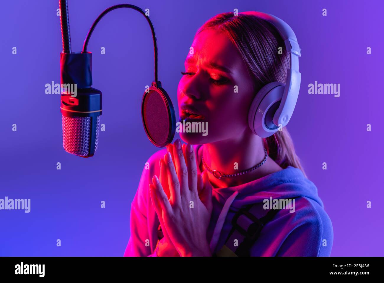 Junge Frau mit kabellosen Kopfhörern, die beim Singen Lieder aufzeichnet Violett mit Farbfilter Stockfoto