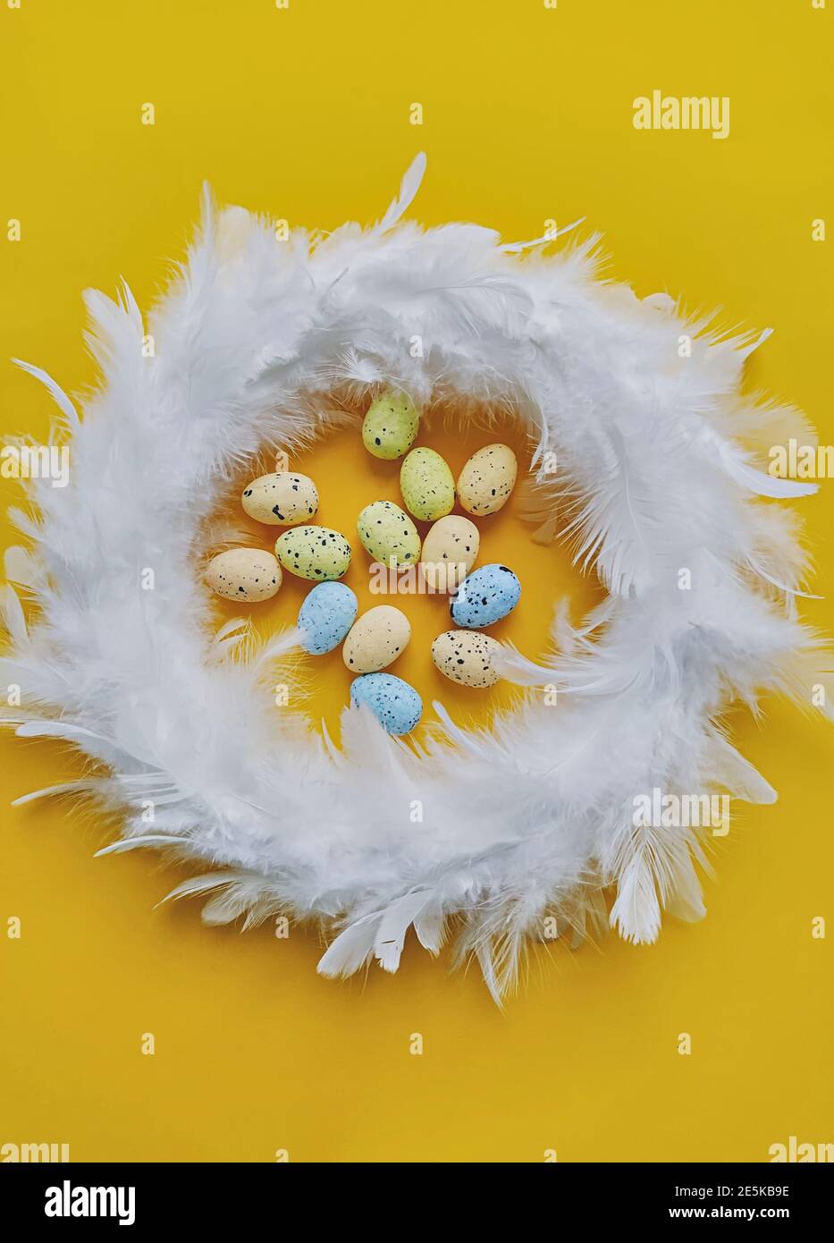 Weißer Federkranz auf gelbem Hintergrund mit Mini-künstlichen Eiern, Draufsicht. Osterdekoration Konzept Stockfoto