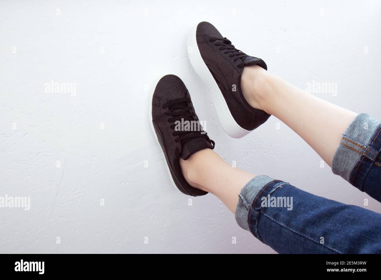 Weibliche Füße von oben gesehen. Selfie für jeden Einsatz. Fuß und Beine in schwarzen Sneakers und Jeans. Fuß an einer weißen Wand angehoben. Mit Kopierbereich. Füße draußen Stockfoto