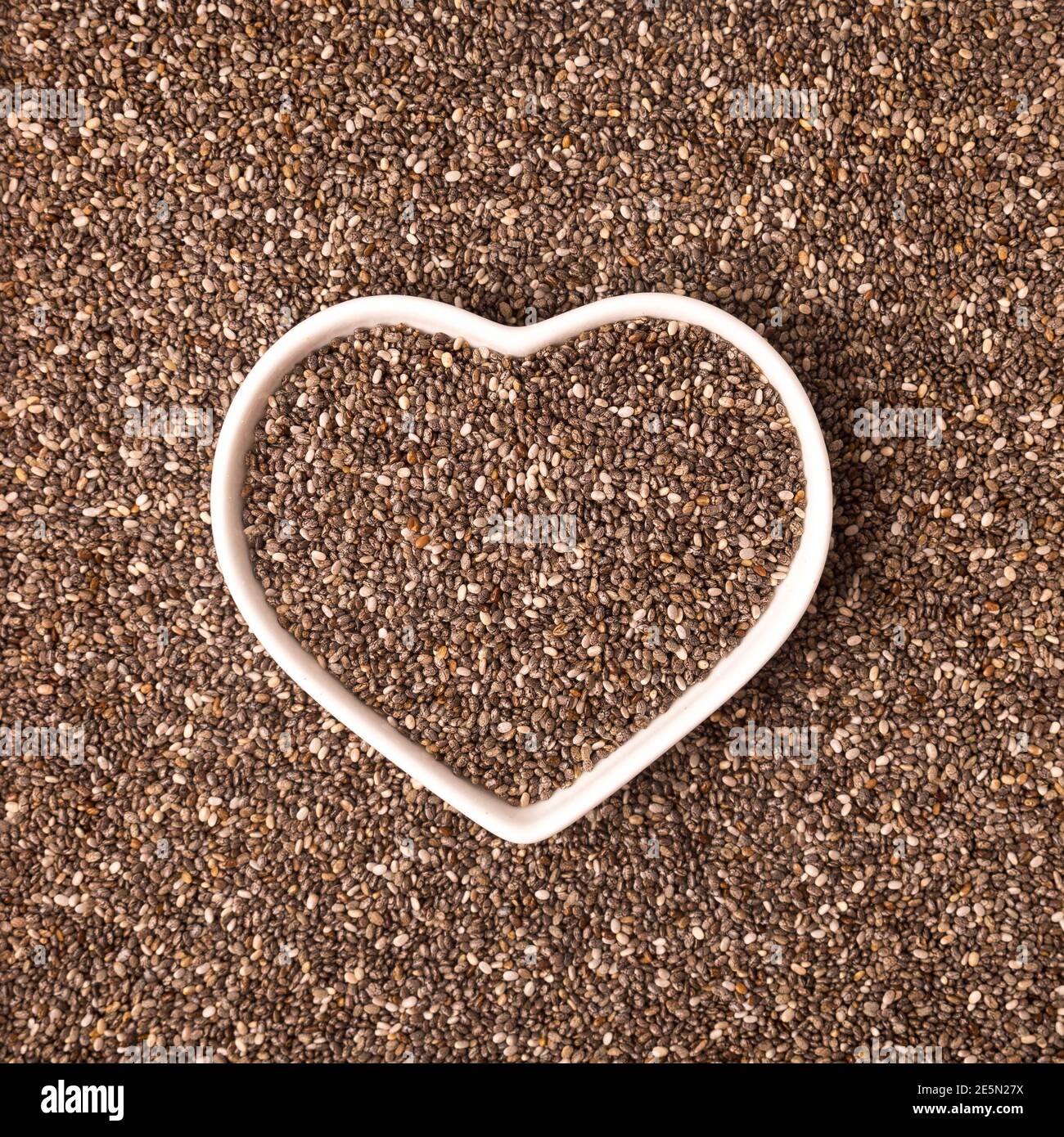 Herzförmige Schale mit Chia-Samen auf Chia-Hintergrund. Glutenfreie und gesunde Ernährung. Ich liebe Chia Samen Konzept. Speicherplatz kopieren Stockfoto